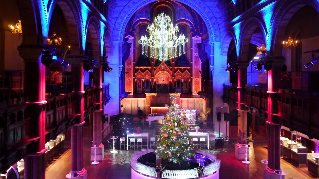 Church event venue transformed with blue and pink architectural lighting, a crystal chandelier and a Christmas tree bar